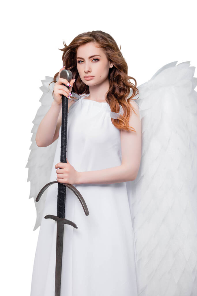 Uma jovem mulher, um anjo com asas em um vestido branco com cabelo voador posando com uma espada em suas mãos isolado em um fundo branco
. - Foto, Imagem