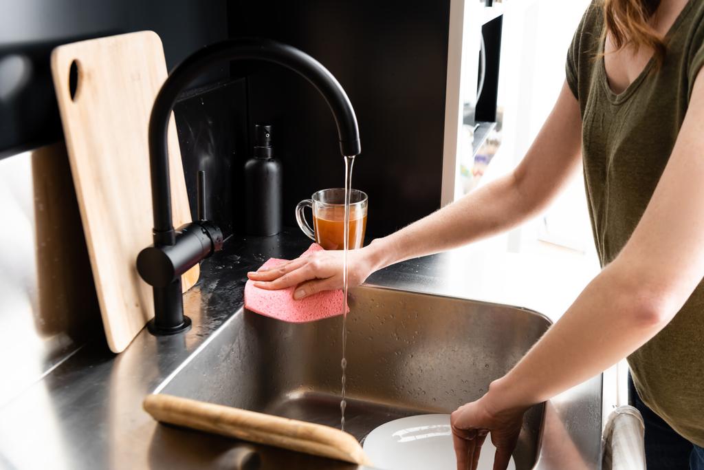 Обрезанный вид женщины, убирающей кухонную раковину тряпкой
  - Фото, изображение