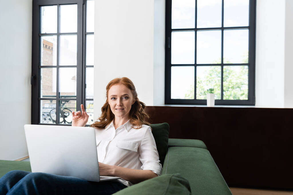 Valikoiva painopiste nainen osoittaa sormella, kun käytät kannettavaa tietokonetta sohvalla kotona  - Valokuva, kuva