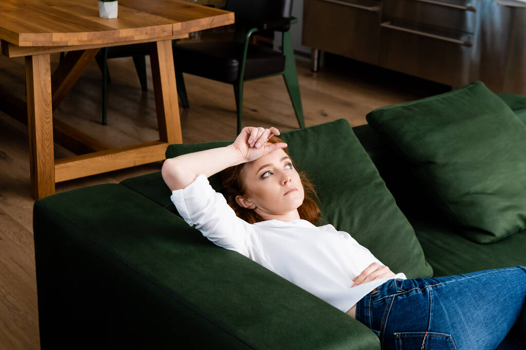 Απογοητευμένη γυναίκα με το χέρι κοντά στο μέτωπο ξαπλωμένη στον καναπέ στο σπίτι  - Φωτογραφία, εικόνα