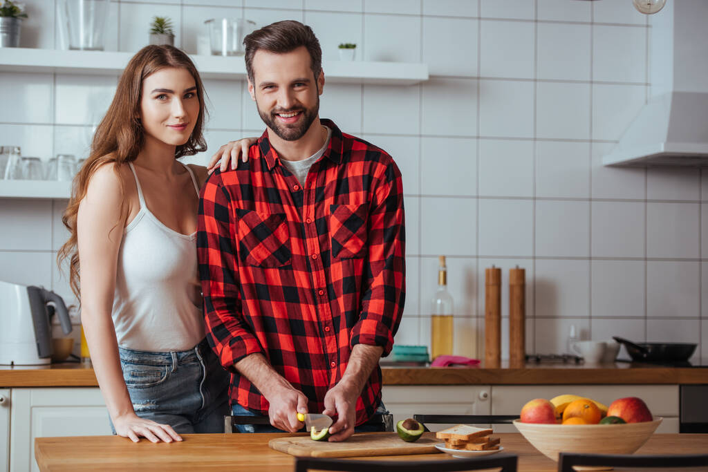 happy young couple smiling at camera while preparing breakfast with fresh fruits together - Photo, Image