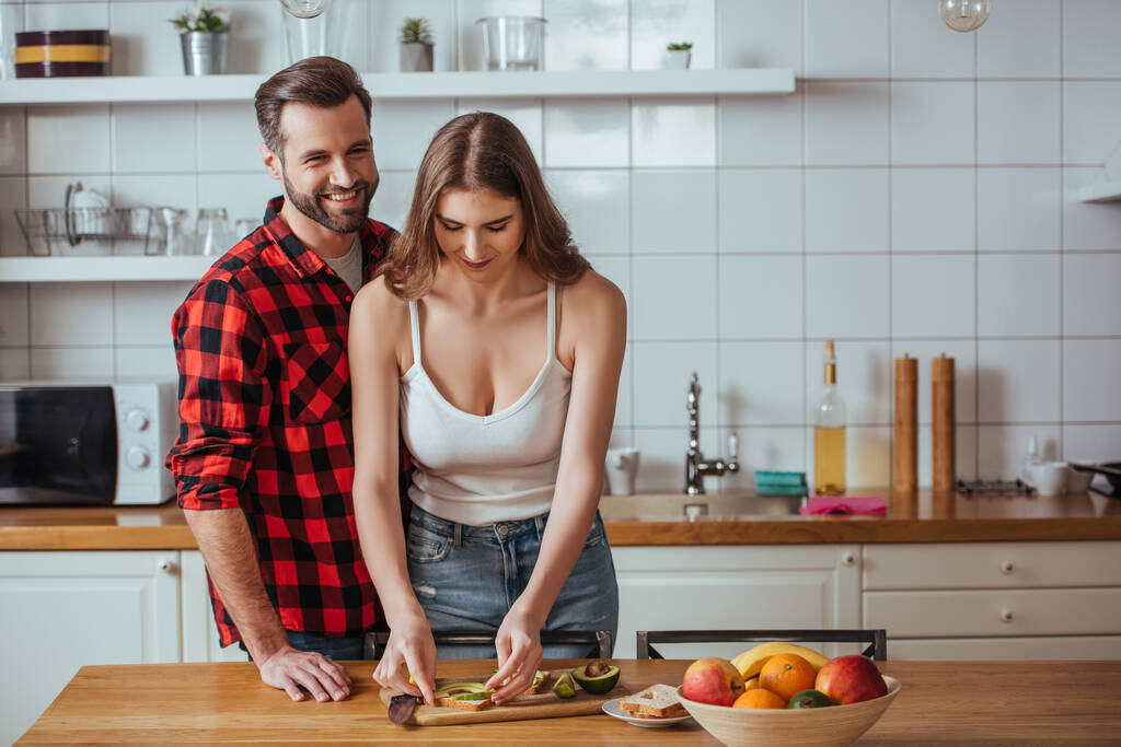 boldog férfi néz kamera közelében vonzó barátnő készít reggelit friss gyümölcsökkel - Fotó, kép