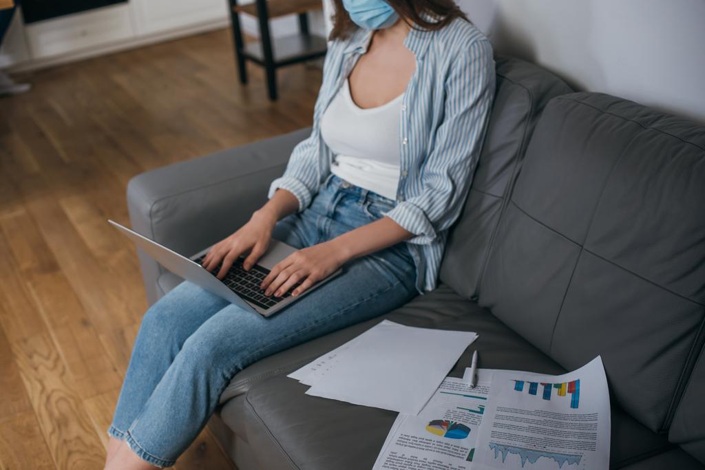 cropped view of young freelancer in medical mask working on sofa at home - Photo, Image