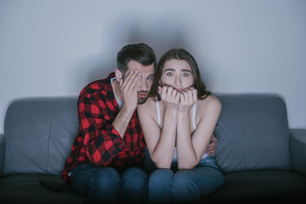 scared man covering eye with hand while watching movie near frightened girl - Photo, Image