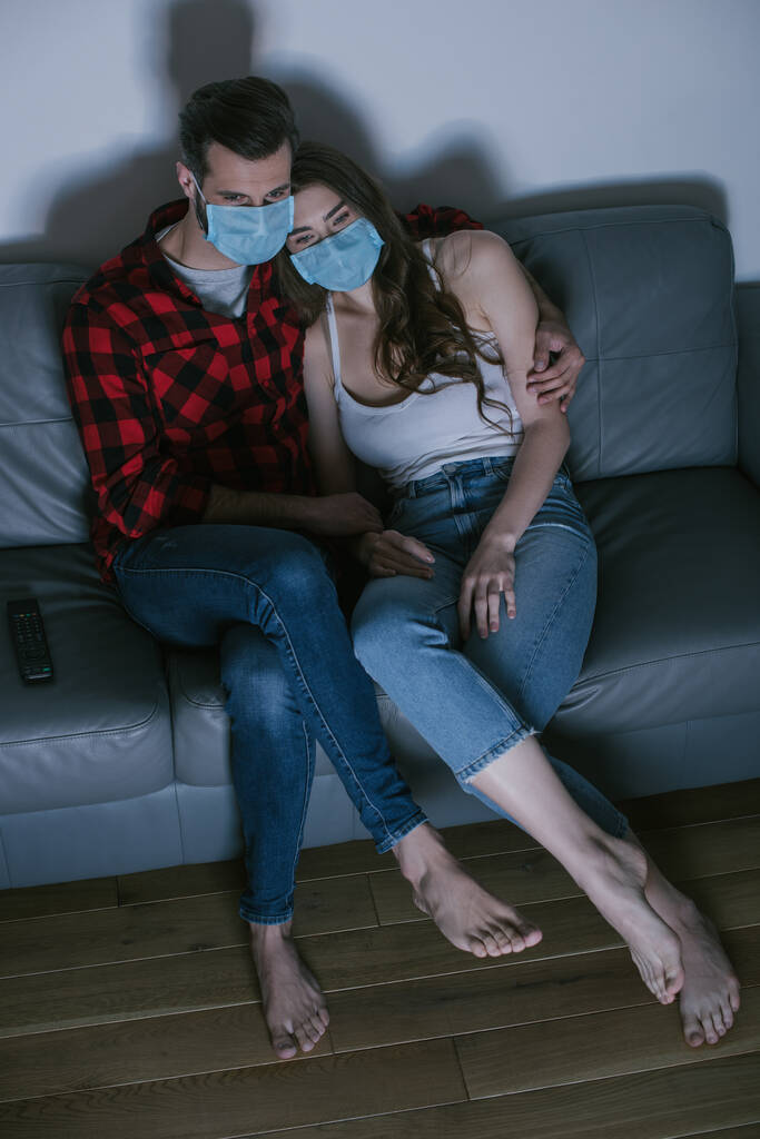 θέα υψηλής γωνίας του νεαρού ζευγαριού με ιατρικές μάσκες βλέποντας τηλεόραση  - Φωτογραφία, εικόνα