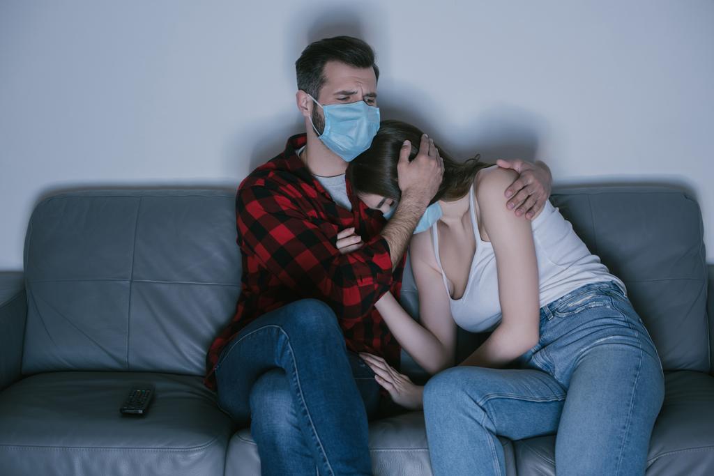jeune couple dans des masques médicaux regarder la télévision tandis que l'homme calme fille bouleversée - Photo, image