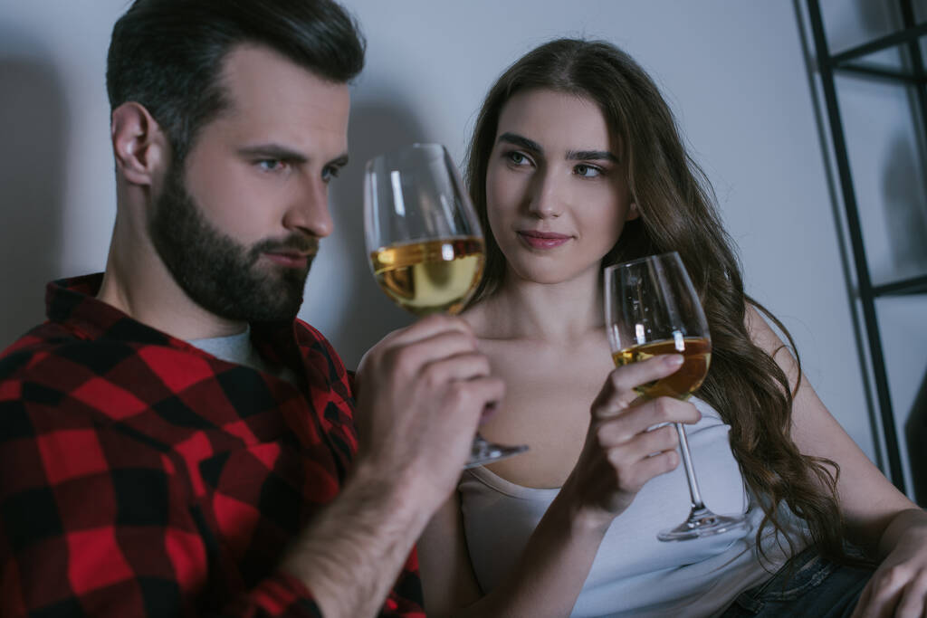lächelndes Mädchen, das seinen verträumten Freund ansieht, während es mit einem Glas Weißwein zusammensitzt - Foto, Bild