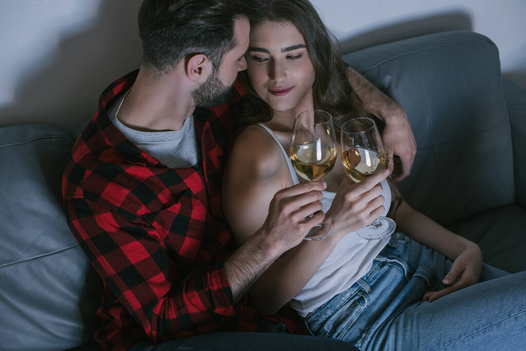 θέα υψηλής γωνίας του ευτυχισμένου ζευγαριού clinking ποτήρια λευκό κρασί, ενώ κάθεται στον καναπέ - Φωτογραφία, εικόνα