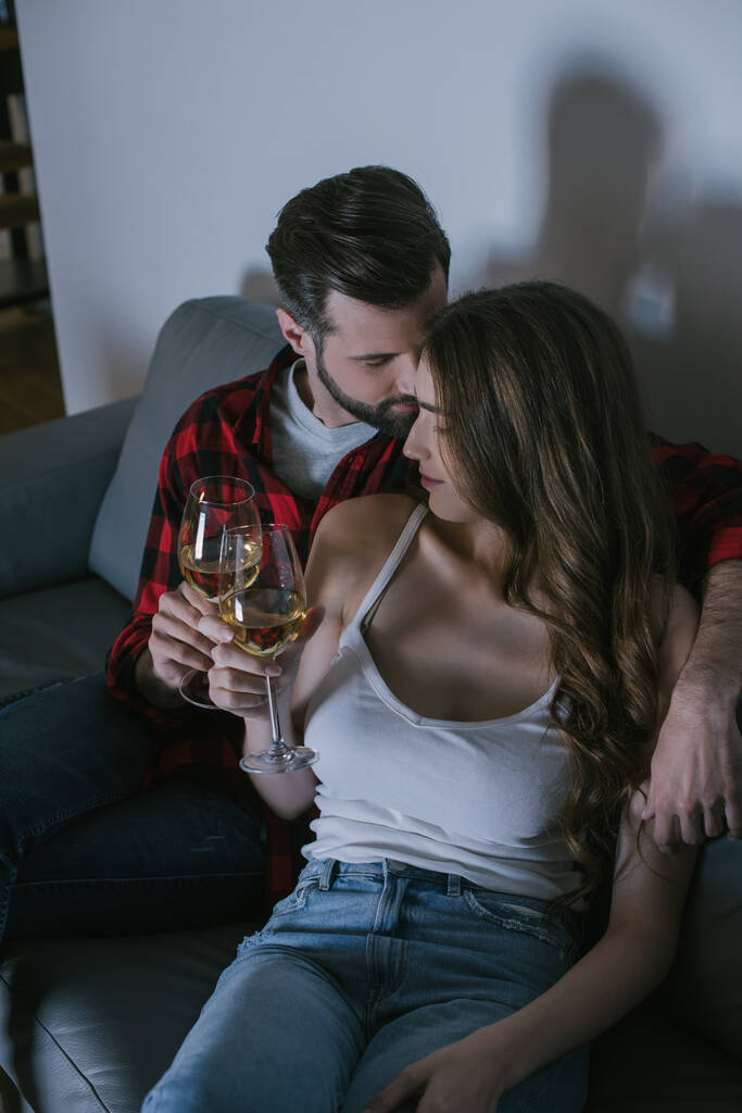 Blick aus der Vogelperspektive auf ein glückliches junges Paar, das mit einem Glas Weißwein auf der Couch sitzt - Foto, Bild