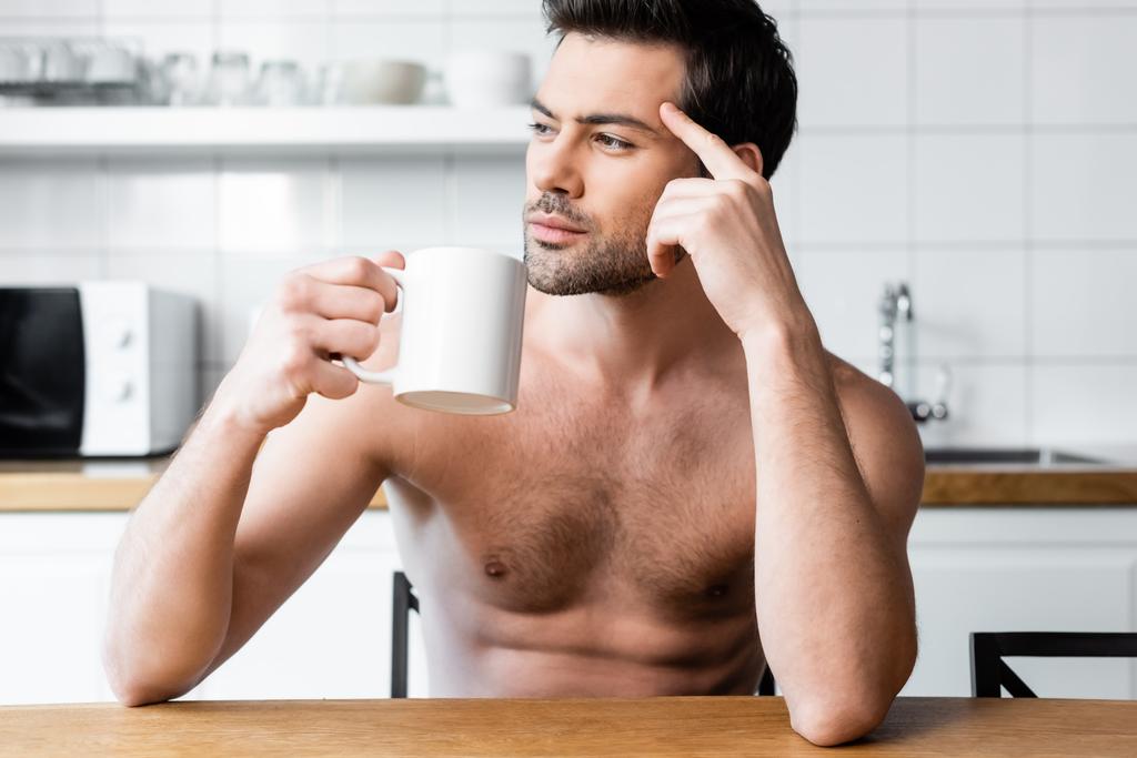 вдумливий без сорочки чоловік тримає чашку кави на кухні вранці
 - Фото, зображення
