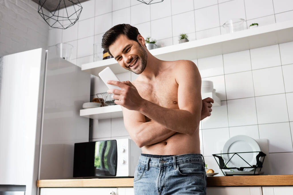 σέξι άνθρωπος γέλιο χρησιμοποιώντας smartphone στην κουζίνα στο σπίτι - Φωτογραφία, εικόνα