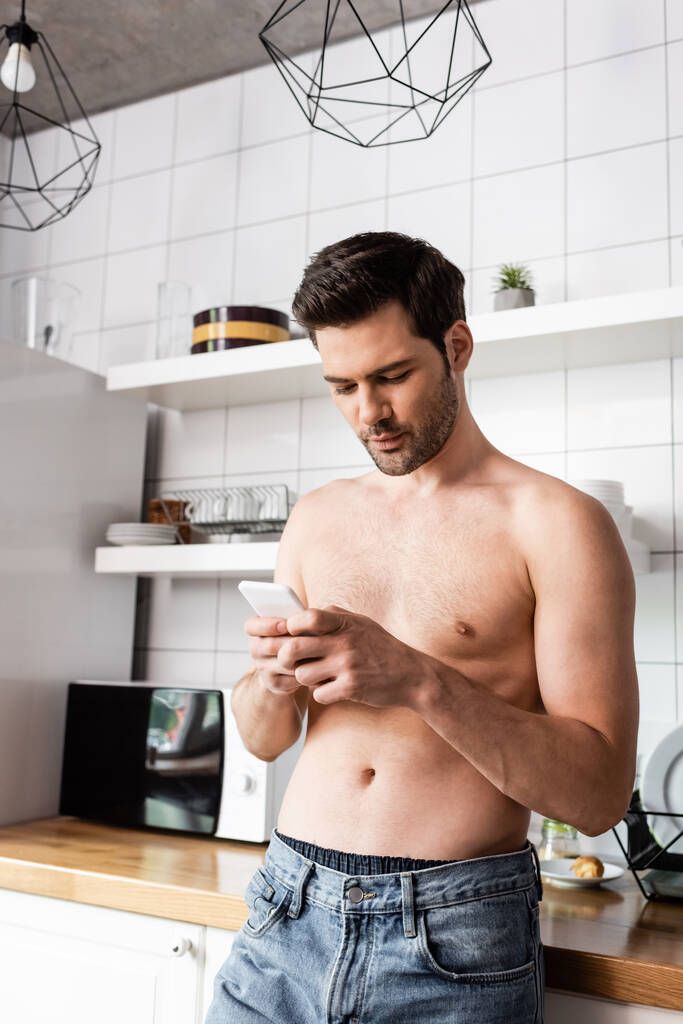 красивый мужчина без рубашки с помощью смартфона на кухне дома
 - Фото, изображение