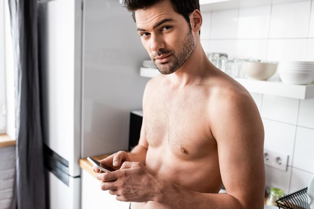 σέξι shirtless άνθρωπος χρησιμοποιώντας smartphone στην κουζίνα στο σπίτι - Φωτογραφία, εικόνα