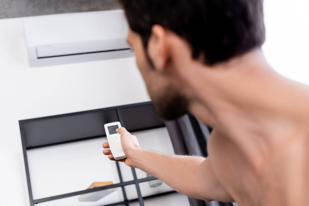 selectieve focus van shirtloze man met afstandsbediening insteltemperatuur van airconditioner thuis - Foto, afbeelding