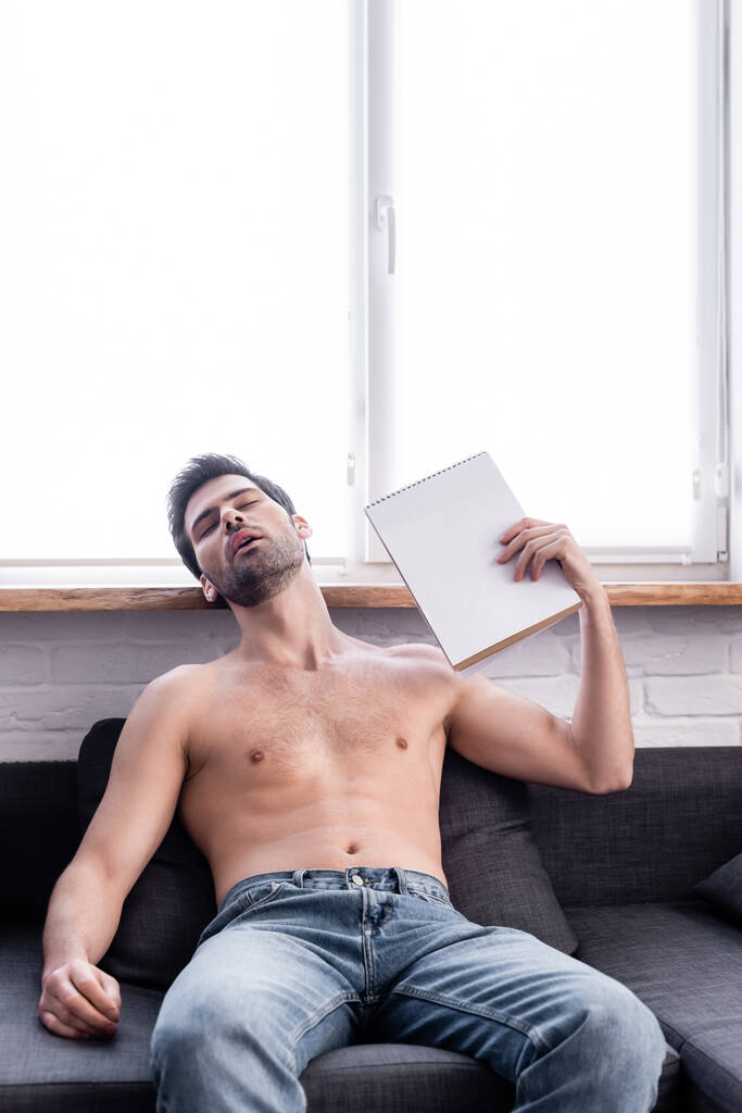 bez koszulki mężczyzna macha notatnikiem jako wentylator podczas gdy cierpi z powodu ciepła w domu - Zdjęcie, obraz