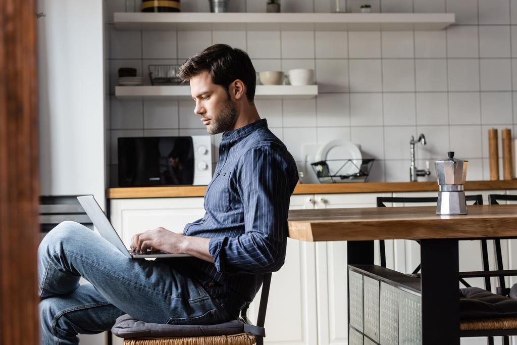 όμορφος ελεύθερος επαγγελματίας εργασίας laptop με κενή οθόνη στην κουζίνα με καφετιέρα κατά τη διάρκεια της αυτο-απομόνωσης   - Φωτογραφία, εικόνα