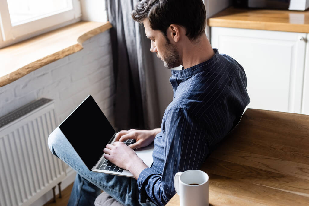 hombre guapo de red portátil con pantalla en blanco en la cocina con taza de café durante la cuarentena
   - Foto, imagen