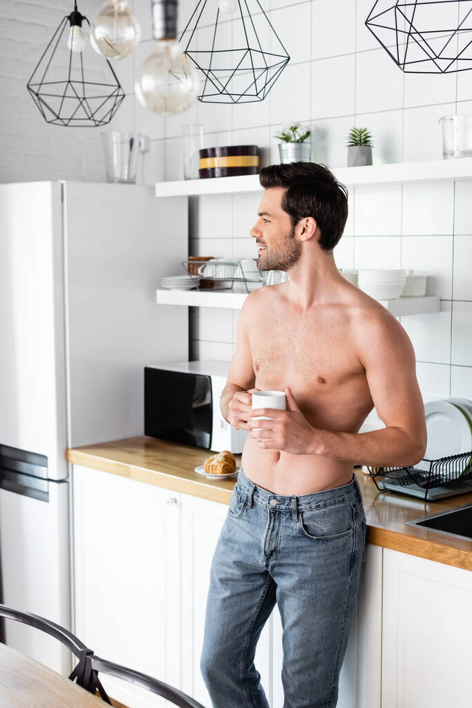усміхнений без сорочки чоловік тримає чашку кави на кухні вранці
 - Фото, зображення