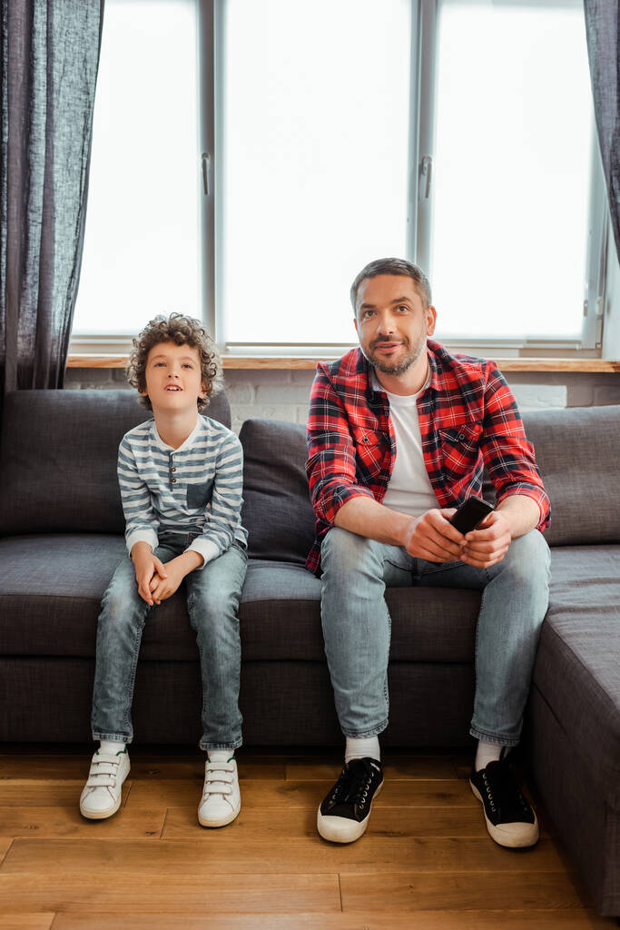 jóképű apa és göndör fiú filmet néz a nappaliban  - Fotó, kép