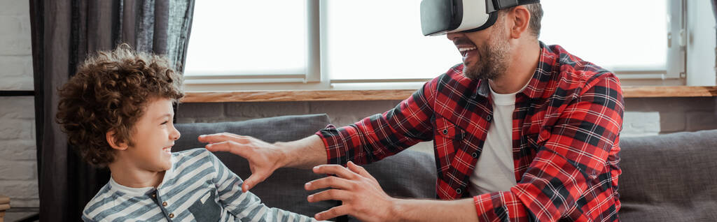horizontální plodina veselého otce ve virtuální realitě headset gestikulující blízko šťastný syn - Fotografie, Obrázek