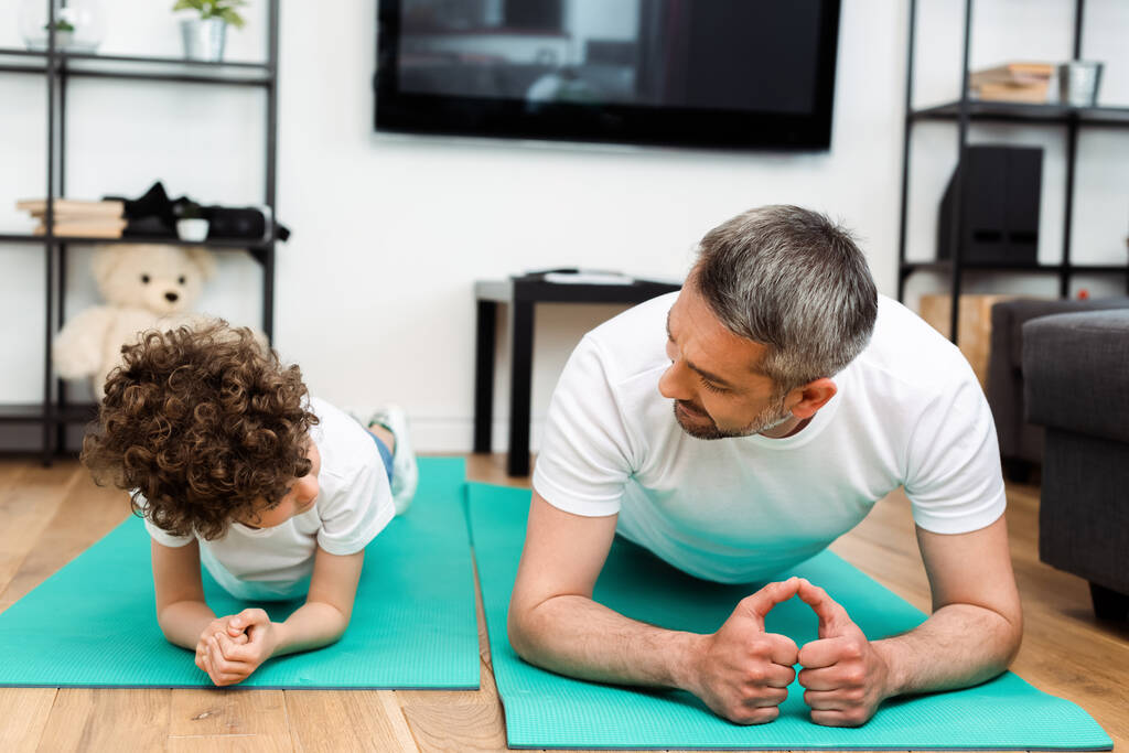 szakállas apa és göndör fiú gyakorló fitness szőnyeg  - Fotó, kép