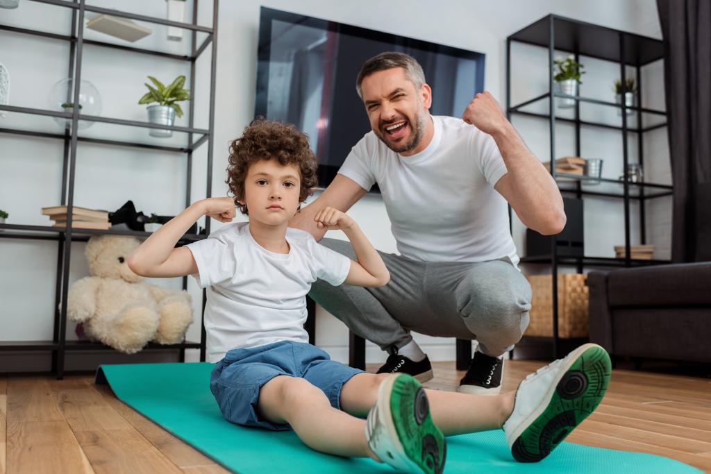 happy father cheering near curly son showing muscle  - Photo, Image