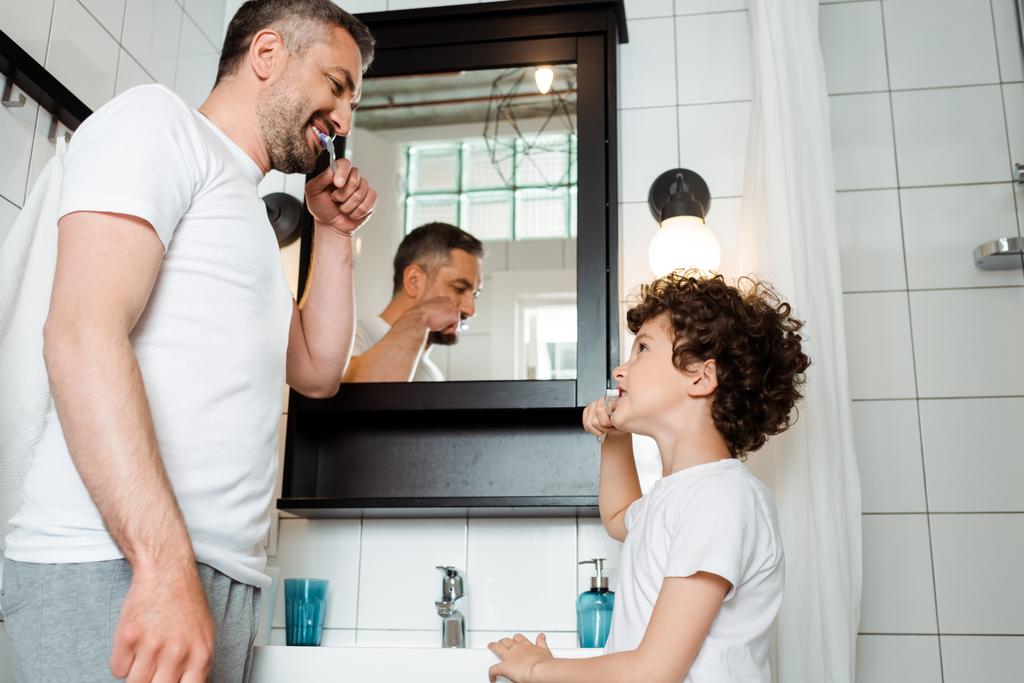 ハンサムな父親と巻き毛の歯をバスルームでブラッシング  - 写真・画像