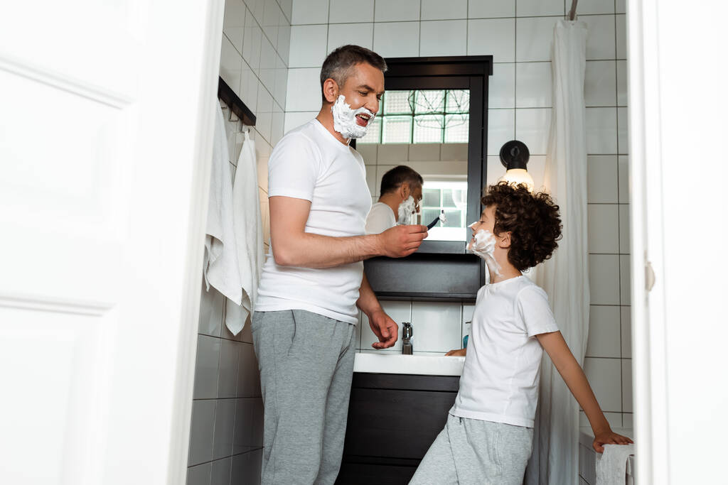bonito pai com espuma de barbear no rosto segurando navalha perto bonito filho
  - Foto, Imagem