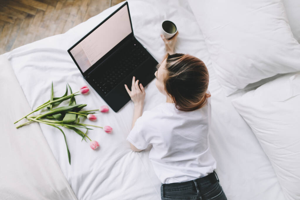 Fiatal nő dolgozik laptop az ágyban fehér vászon. Életmód kompozíció. Otthon dolgozni, karantén koncepció.  - Fotó, kép