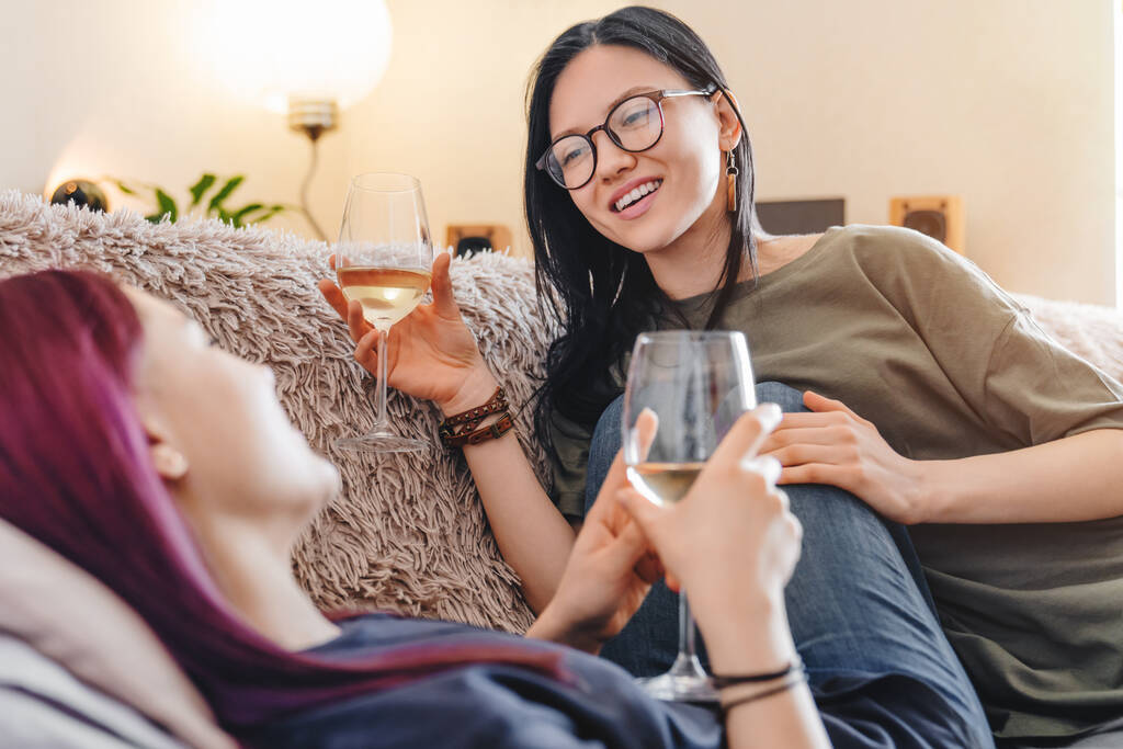 Ευτυχισμένο νεαρό λεσβιακό ζευγάρι με ποτήρια κρασιού στον καναπέ στο σπίτι - Φωτογραφία, εικόνα