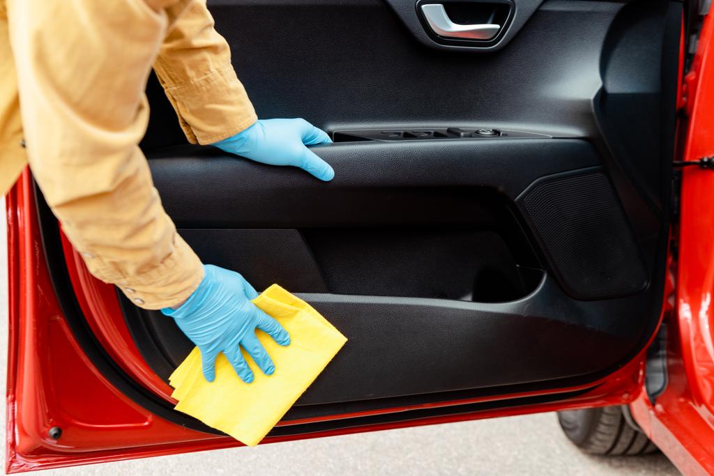Lastik eldivenli bir adamın covid-19 salgını sırasında arabanın kapılarını paçavrayla temizlerken görüntüsü. - Fotoğraf, Görsel