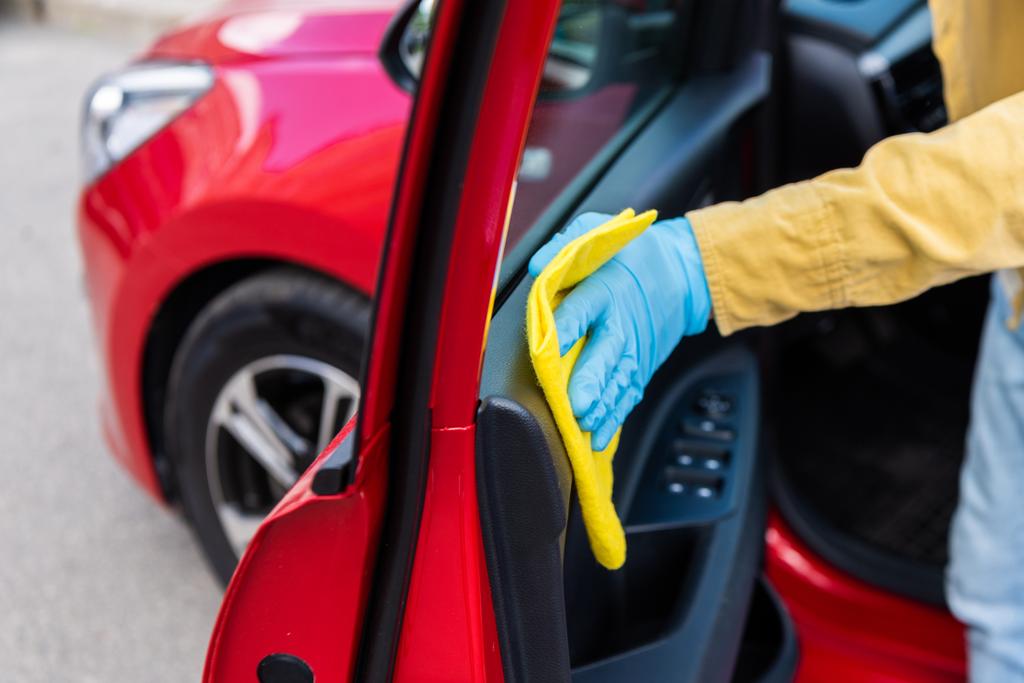 частичное представление человека в медицинских перчатках, чистящих двери автомобиля с тряпкой во время пандемии коронавируса
 - Фото, изображение