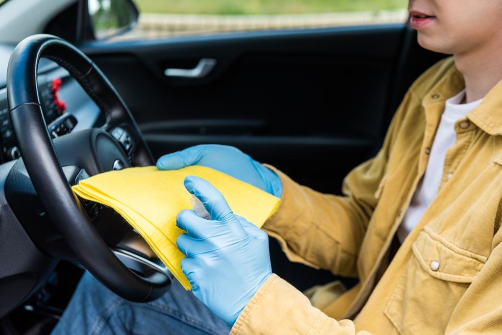 vista recortada del hombre en guantes de látex usando antiséptico y trapo para la desinfección interior del coche durante la pandemia de covid-19
 - Foto, imagen