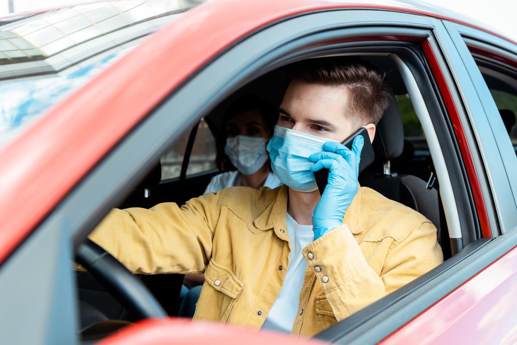 motorista masculino em máscara médica e luvas conversando ao telefone em táxi com passageiro durante pandemia de coronavírus
 - Foto, Imagem