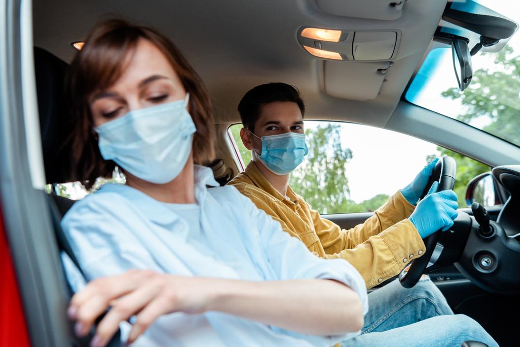 man and woman in medical masks and protection gloves sitting in car during coronavirus pandemic, selective focus - Photo, Image