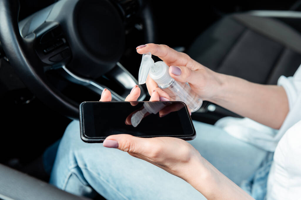 oříznutý pohled na ženu používající antiseptika pro smartphone v autě během pandemie koronaviru - Fotografie, Obrázek
