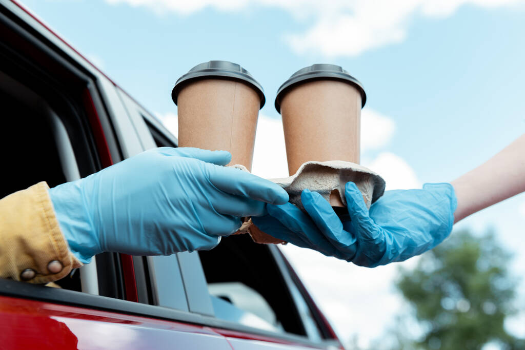コロナウイルスのパンデミックの際に車からコーヒーを購入する保護手袋の男のクロップドビュー  - 写真・画像