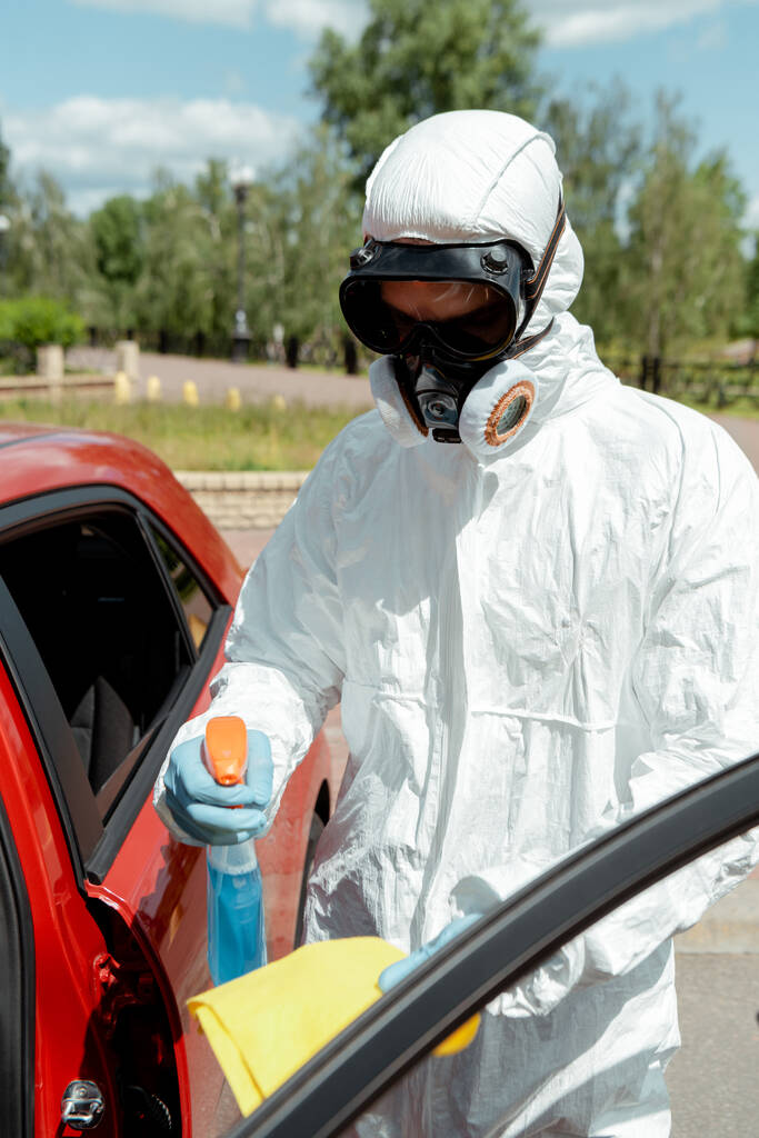 limpiador en traje de hazmat coche de limpieza con spray antiséptico y trapo durante la pandemia coronavirus
 - Foto, imagen