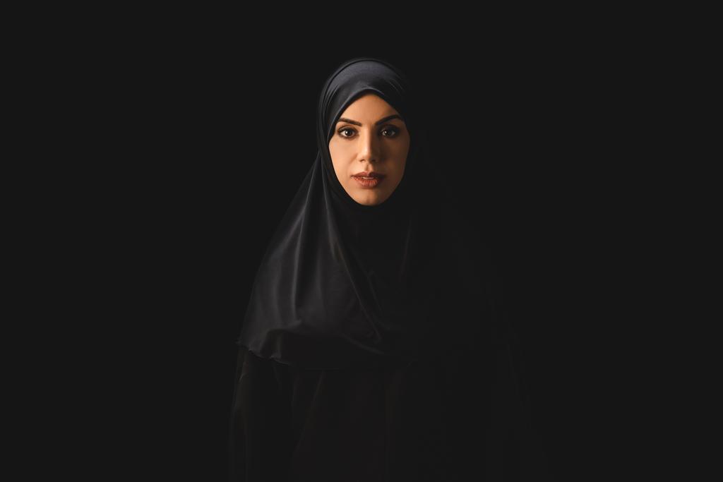 Mooie moslim vrouw op zoek naar camera geïsoleerd op zwart  - Foto, afbeelding