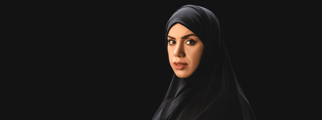 Панорамний знімок мусульманської жінки в хіджабі дивиться на камеру ізольовано на чорному
  - Фото, зображення
