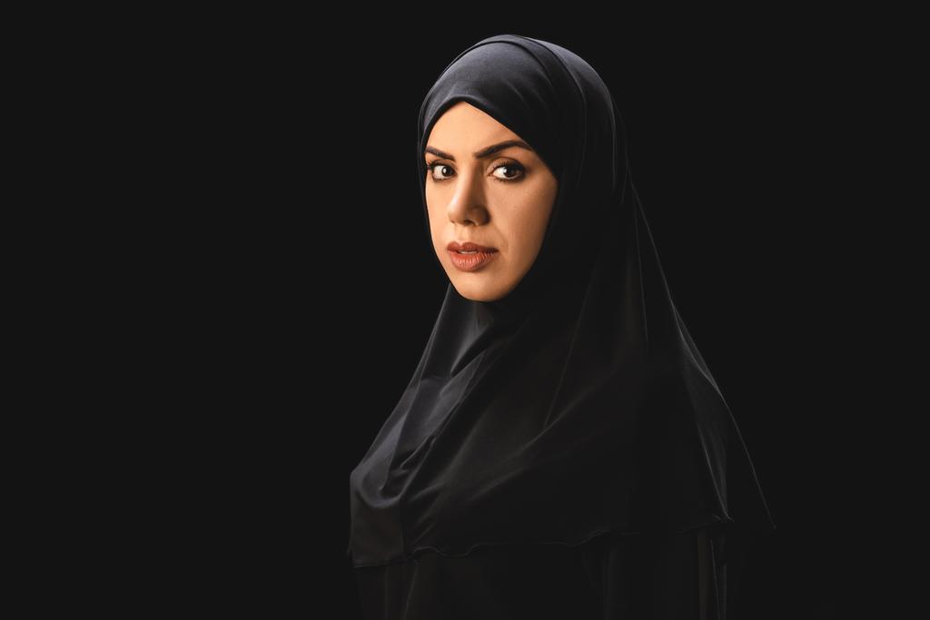 美しいイスラム教徒の女性の側のビューは黒で隔離されたカメラを見て  - 写真・画像