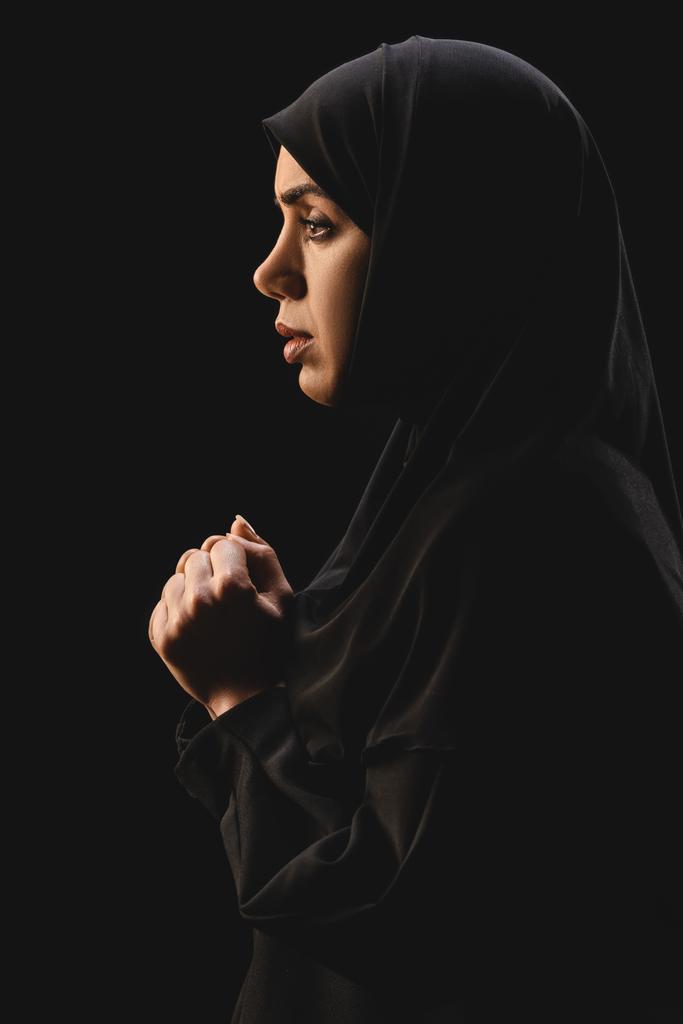Vista lateral do refugiado muçulmano no hijab olhando para longe isolado no preto
  - Foto, Imagem