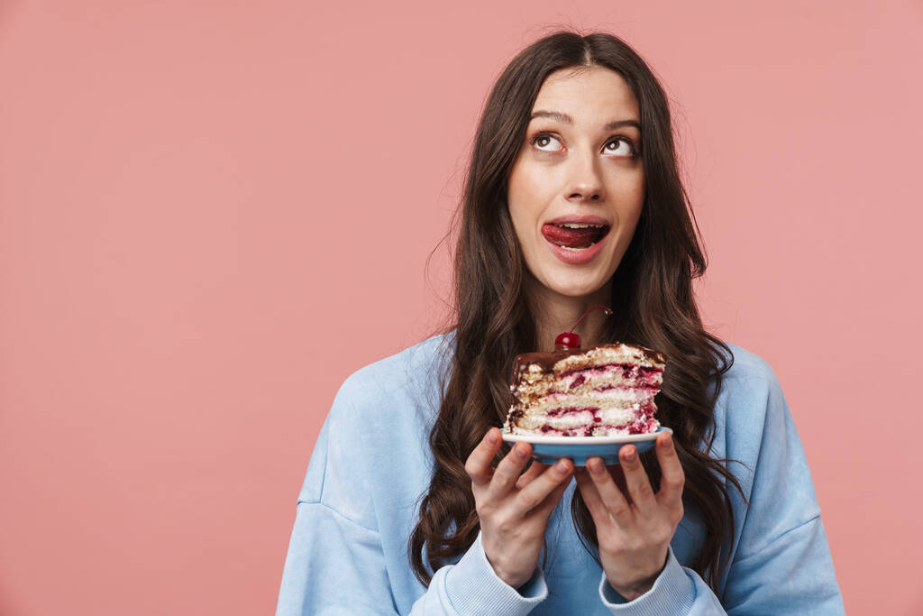 Образ мислення молодої жінки, яка любить губи, тримаючи торт ізольовано на рожевому фоні
 - Фото, зображення
