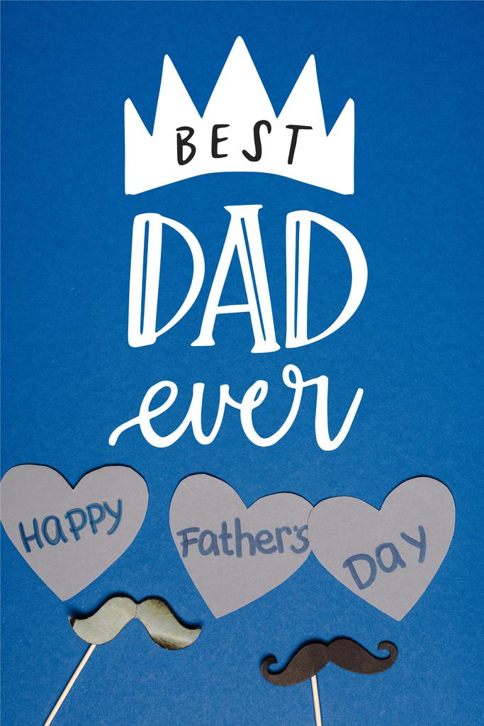 top view διακοσμητικό μαύρο μουστάκι και χαρτί κομμένο γκρι καρδιές με γράμματα ευτυχισμένη ημέρα πατεράδες σε μπλε φόντο, καλύτερη εικόνα μπαμπάς ποτέ - Φωτογραφία, εικόνα