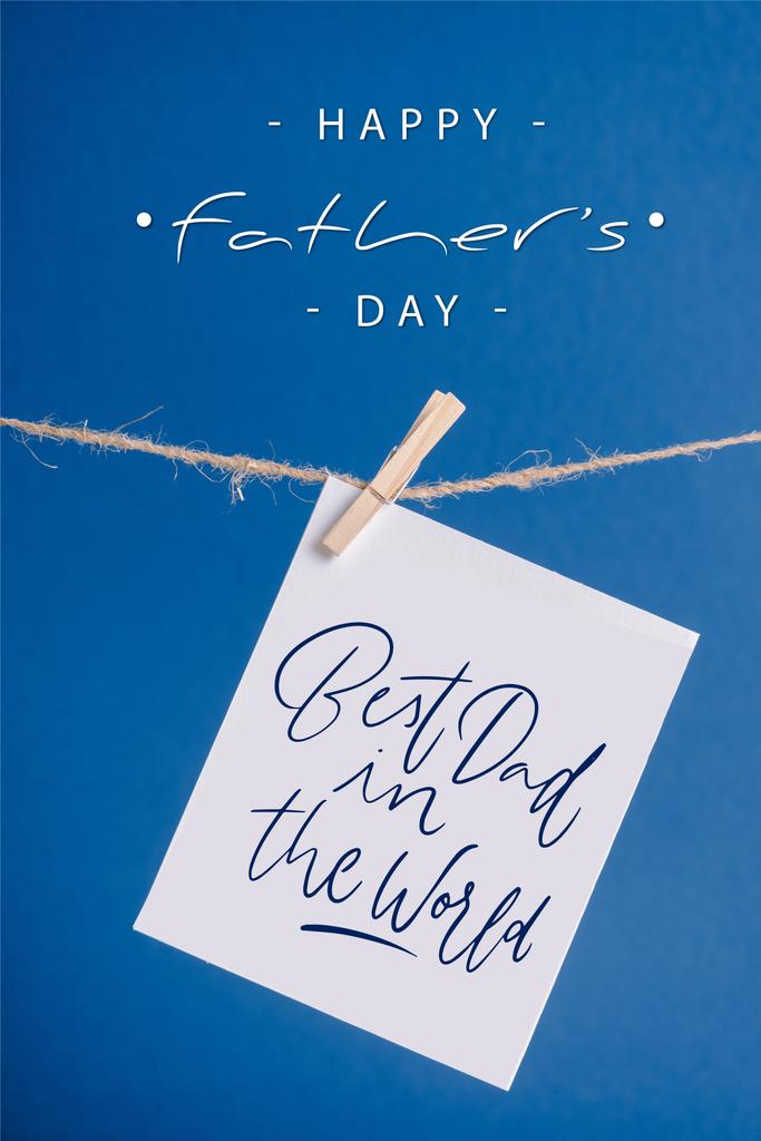 White greeting card with best dad in the world illustration hanging on rope with clothespins isolated on blue - Photo, Image