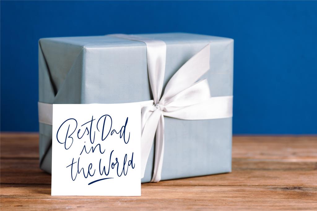selective focus of greeting card with best dad in the world illustration and gift box with white bow isolated on blue - Photo, Image