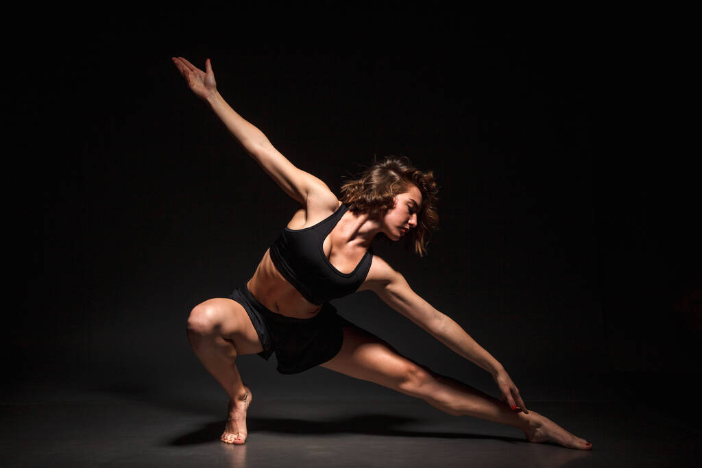 jong meisje doet yoga op een zwarte achtergrond - Foto, afbeelding