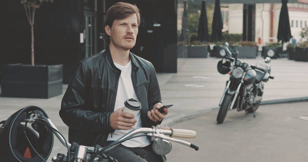 Biker trinkt Kaffee, während er neben Motorrad steht - Foto, Bild