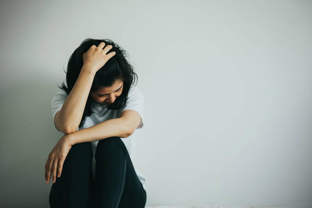 Kobieta z depresją przytula kolano i płacze. Smutna kobieta siedzi sama w pustym pokoju..  - Zdjęcie, obraz