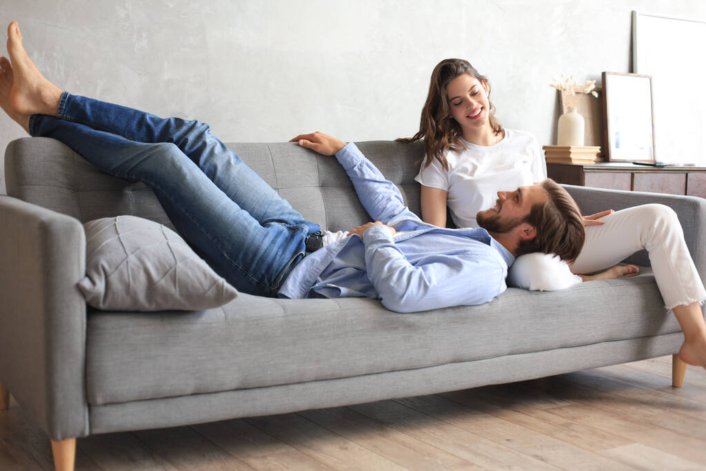Young loving couple relaxing on sofa together, husband lying on wife legs resting on couch, concept of capture happy moment - Photo, Image